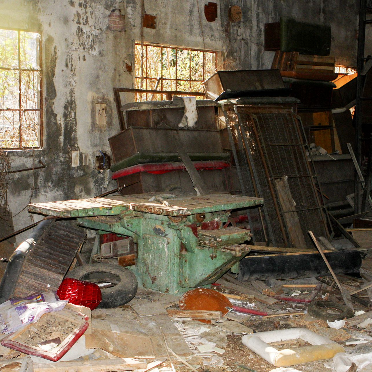 Intérieur délabré d'une pièce, avec une grande table verte usée, des débris et des fenêtres en arrière-plan.