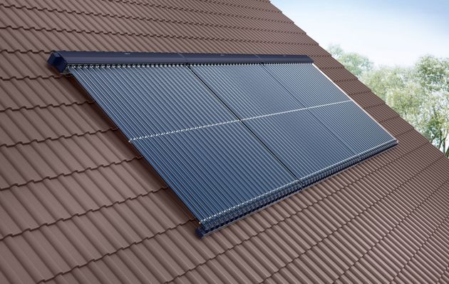 Person inspiziert Solarpaneele mit einer Wärmebildkamera; grüne Weste, weisser Helm.