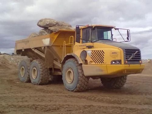 Un camión volquete amarillo está estacionado en un campo de tierra.