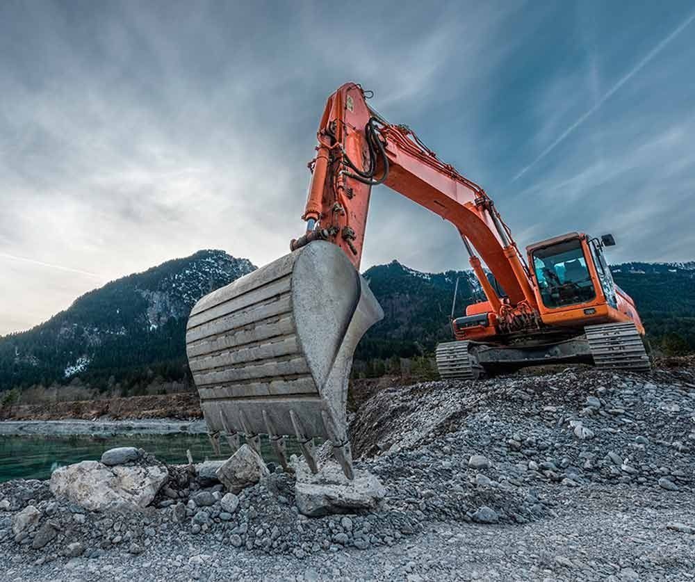 Una gran excavadora naranja está sentada en la cima de una colina rocosa.
