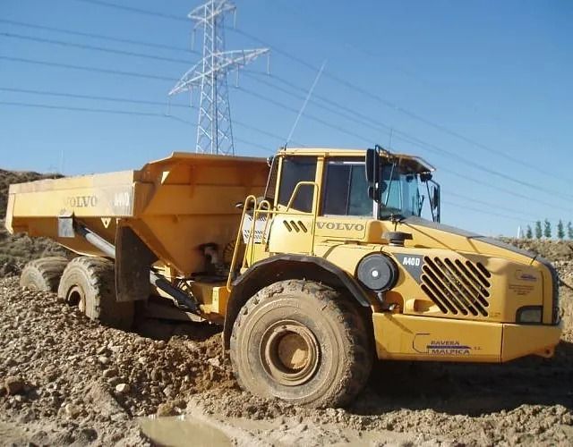 Un camión volquete Volvo amarillo circula por un campo de tierra.