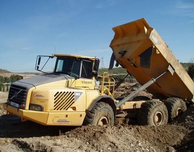 Un camión volquete Volvo conduce por un campo de tierra.