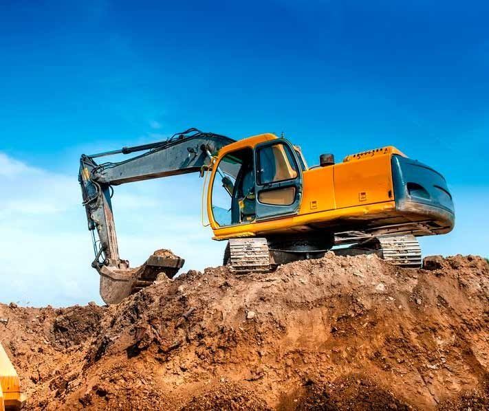 Una excavadora amarilla está sentada encima de una pila de tierra.