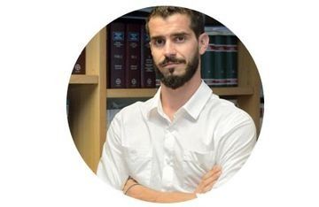 Hombre con barba, camisa blanca, con los brazos cruzados, delante de una estantería.