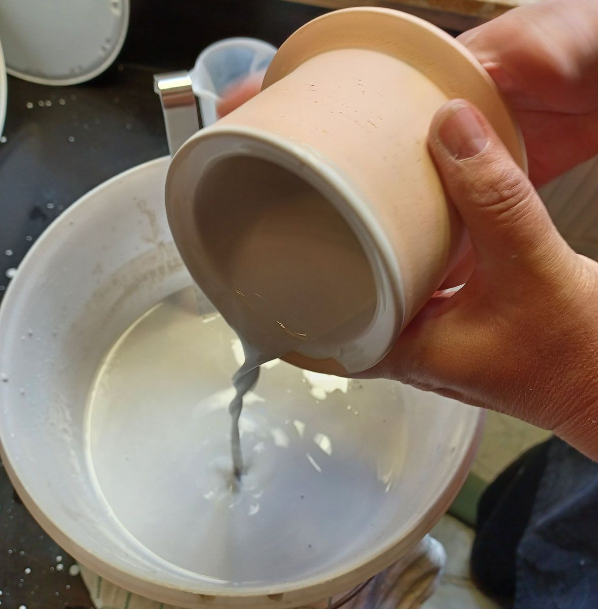 Die dicke Flüssigkeit wird von Hand aus einer beigen Tasse in eine weiße Schüssel gegossen.