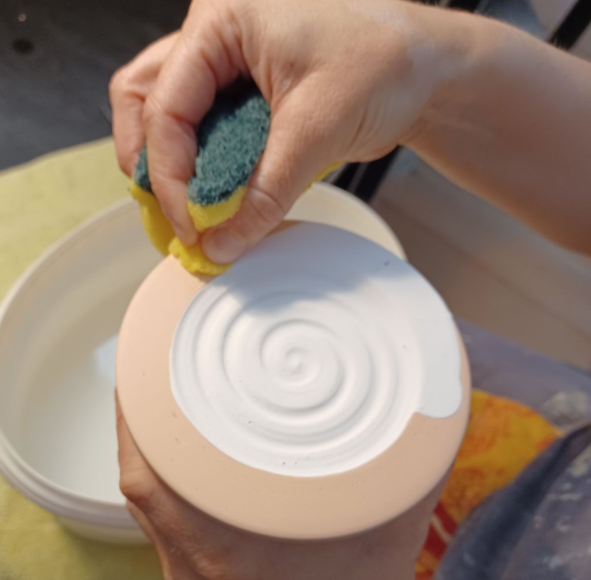 Ich drücke einen Schwamm mit der Hand über einer weißen, spiralförmigen Seifenschale auf einem beigen Becher aus.