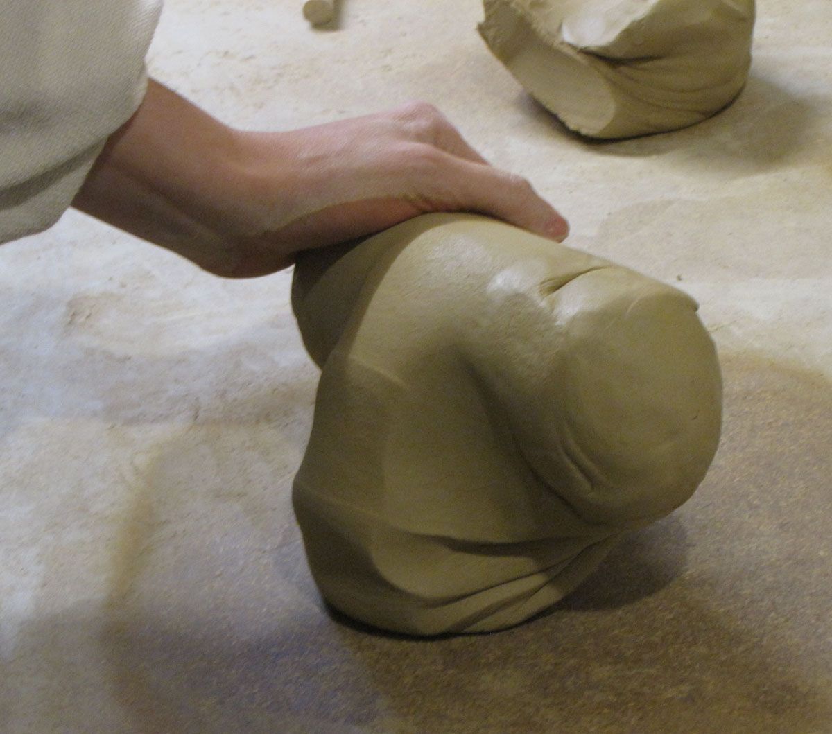 Auf einem Arbeitstisch formt man beigefarbenen Ton von Hand zu einer runden Skulptur.