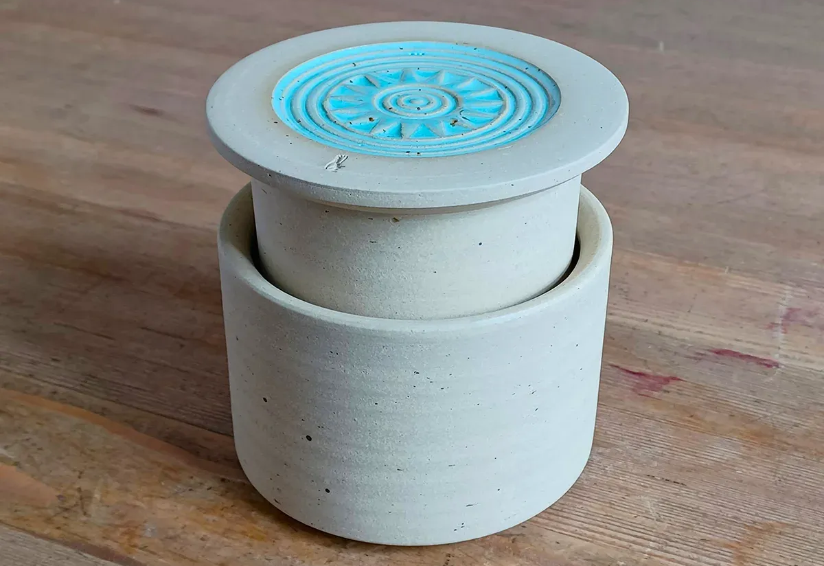 Kleiner beigefarbener Keramikbehälter mit Deckel, der ein blaues Spiralmuster aufweist, auf einer Holzoberfläche