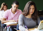 Un grupo de estudiantes están sentados en escritorios en un salón de clases.