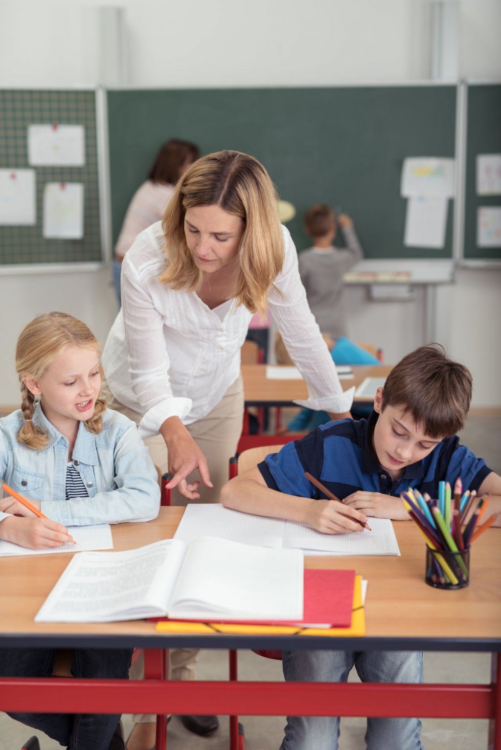 Una maestra está ayudando a sus estudiantes con sus tareas en un salón de clases.