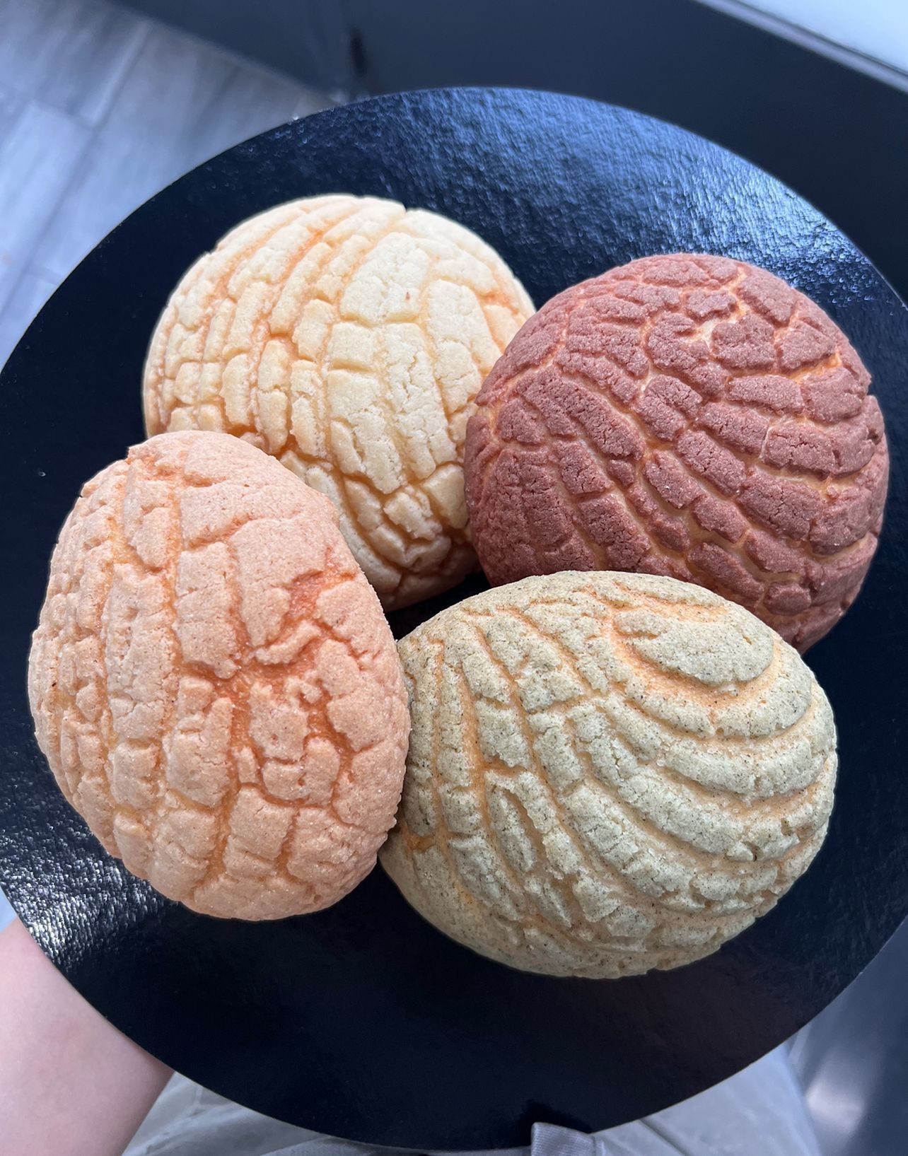 Cuatro galletas coloridas con diferentes diseños sobre un pequeño plato negro, vistas desde arriba.