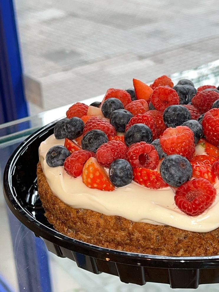 Pastel con cobertura de frutos rojos y glaseado blanco sobre una bandeja negra.
