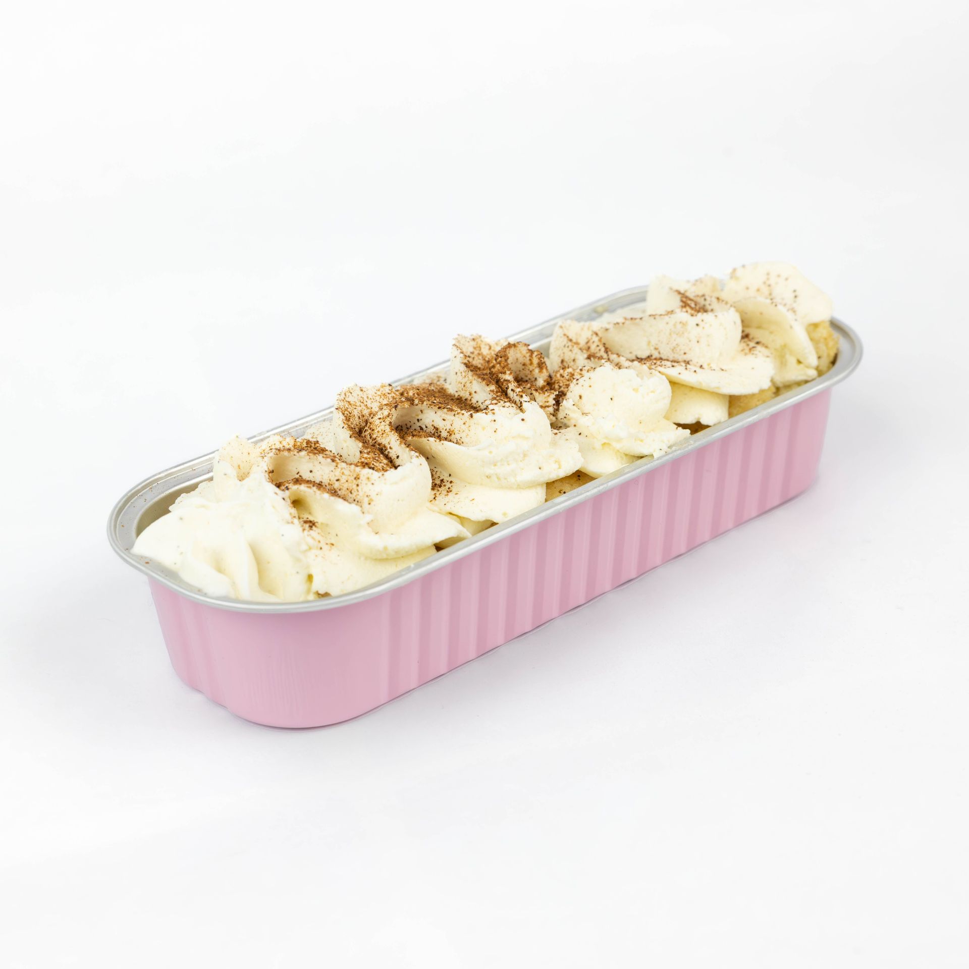 Molde rosa para pan relleno de plátanos en rodajas y cubierto con canela sobre un fondo blanco.