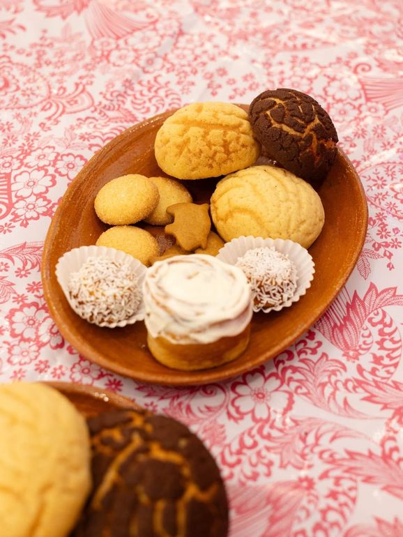 Galletas variadas en un plato de madera sobre un mantel rosa estampado.