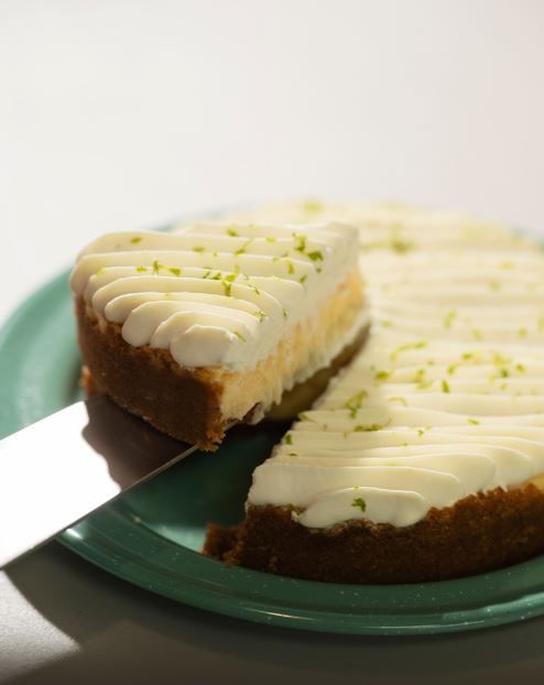 Una porción de pastel con crema sobre un plato verde, adornada con ralladura de lima.