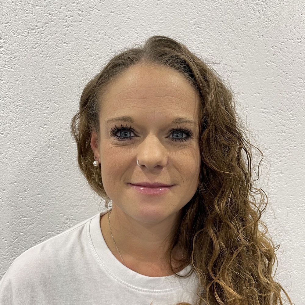 Eine Frau mit langen lockigen Haaren und einem Nasenring trägt ein weißes Hemd.