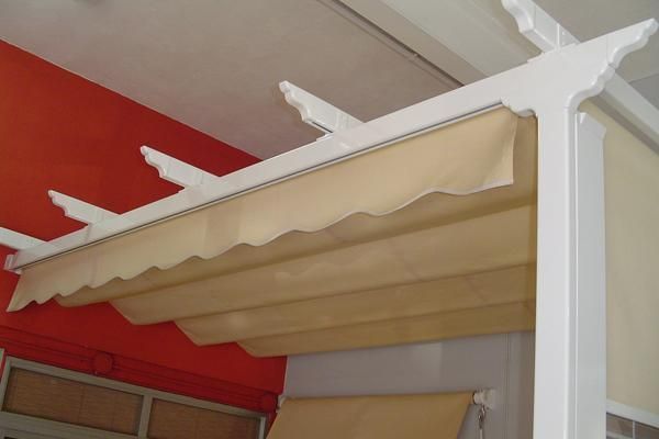 Una pérgola blanca con un toldo beige colgando del techo.
