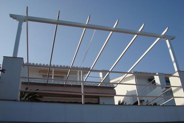 Un balcón con una pérgola blanca encima.