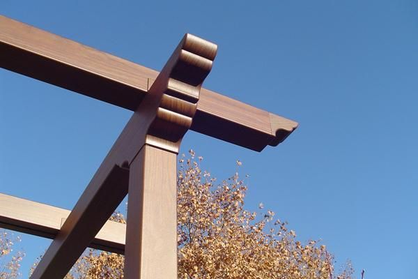 Una pérgola de madera contra un cielo azul con árboles al fondo.