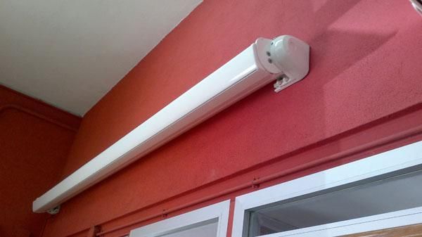 Una lámpara blanca cuelga de una pared roja al lado de una ventana.