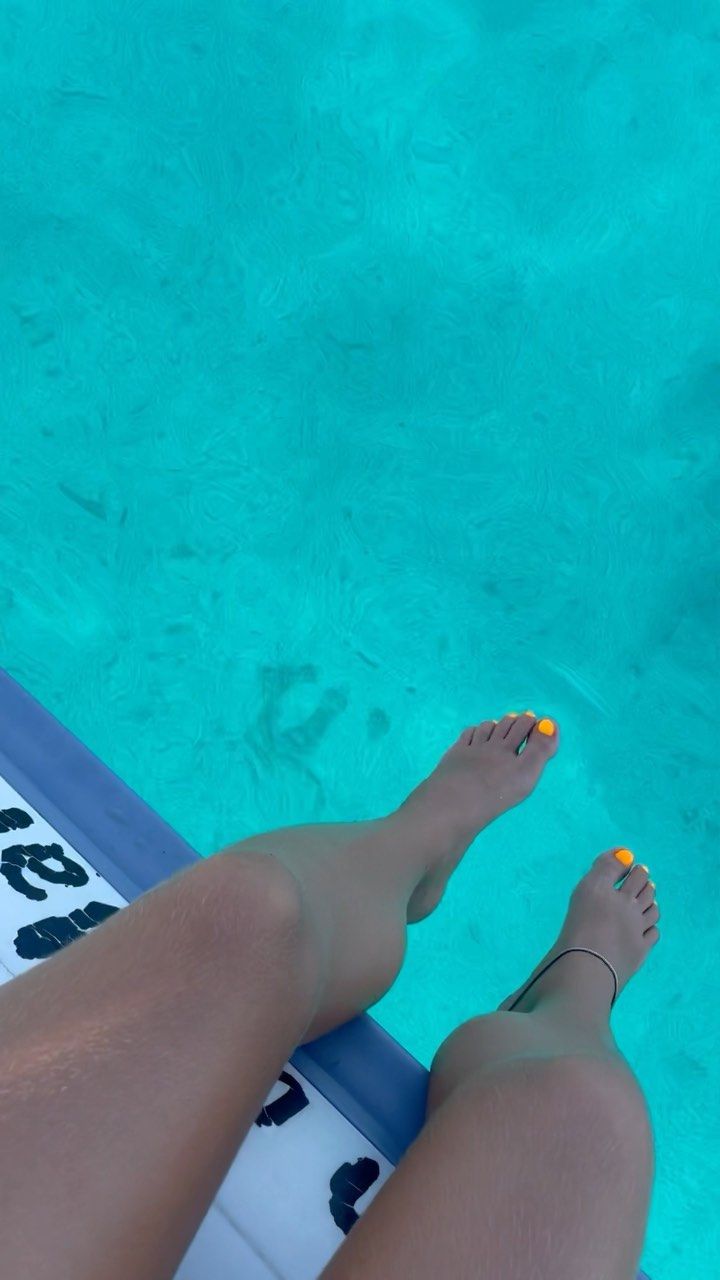 Pies con las uñas pintadas de amarillo brillante colgando sobre aguas de un vibrante color turquesa desde la cubierta de un barco.