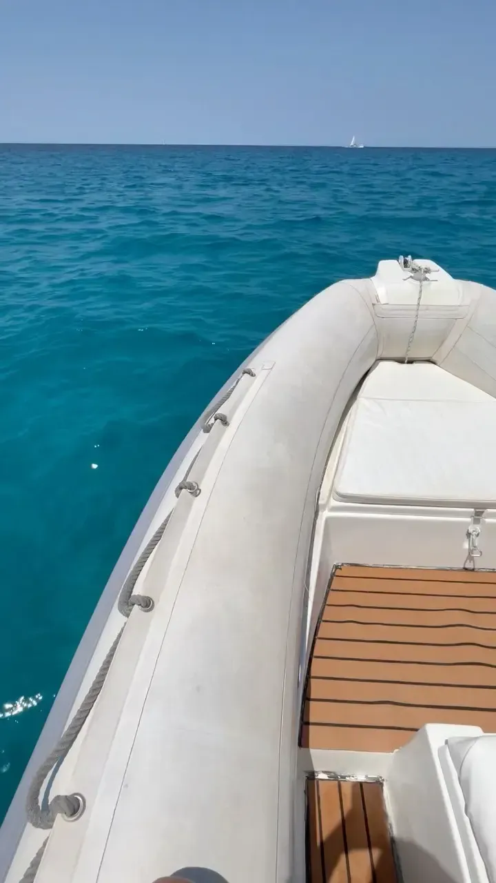 Vista desde la proa de una lancha neumática blanca de casco rígido que se desplaza sobre aguas oceánicas de color turquesa cristalino.