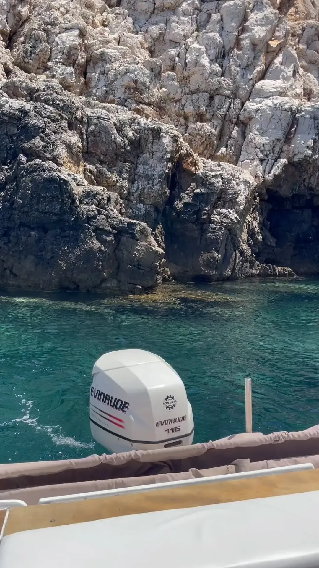 Un motor de barco blanco se alza sobre aguas turquesas, con escarpados acantilados rocosos de color claro como telón de fondo.