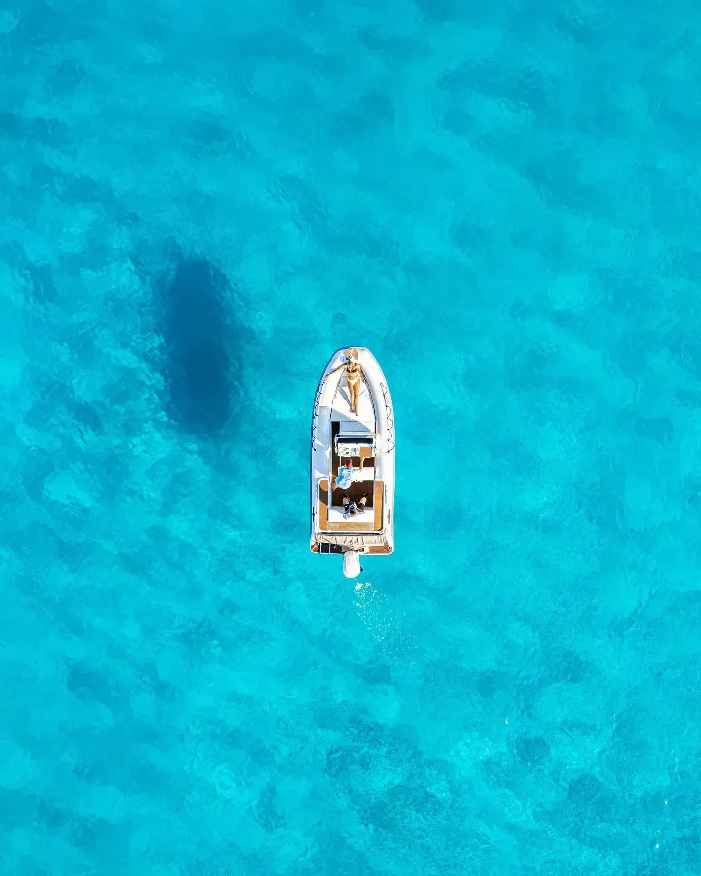 Vista aérea de un barco flotando sobre aguas cristalinas de color turquesa, proyectando una sombra oscura sobre el fondo marino arenoso.