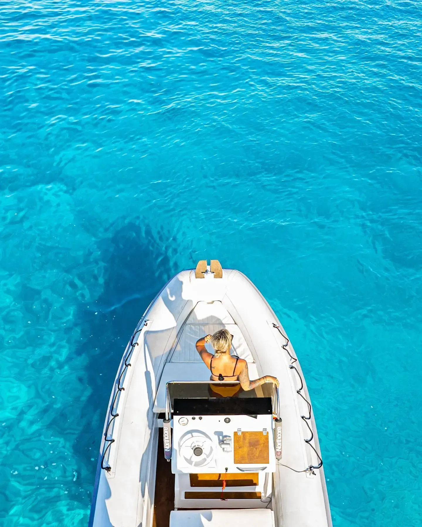 Una toma aérea de una persona conduciendo una pequeña lancha motora blanca a través de aguas turquesas brillantes y cristalinas.