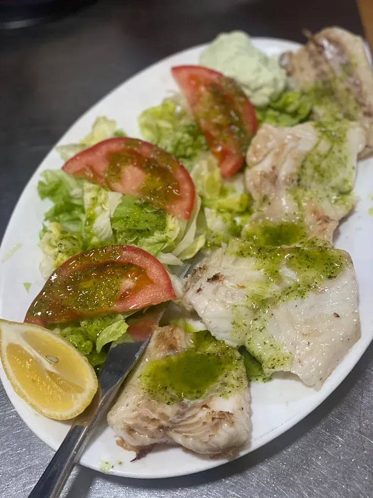 Plato de pescado a la plancha, tomate, lechuga y limón, rociado con salsa verde.
