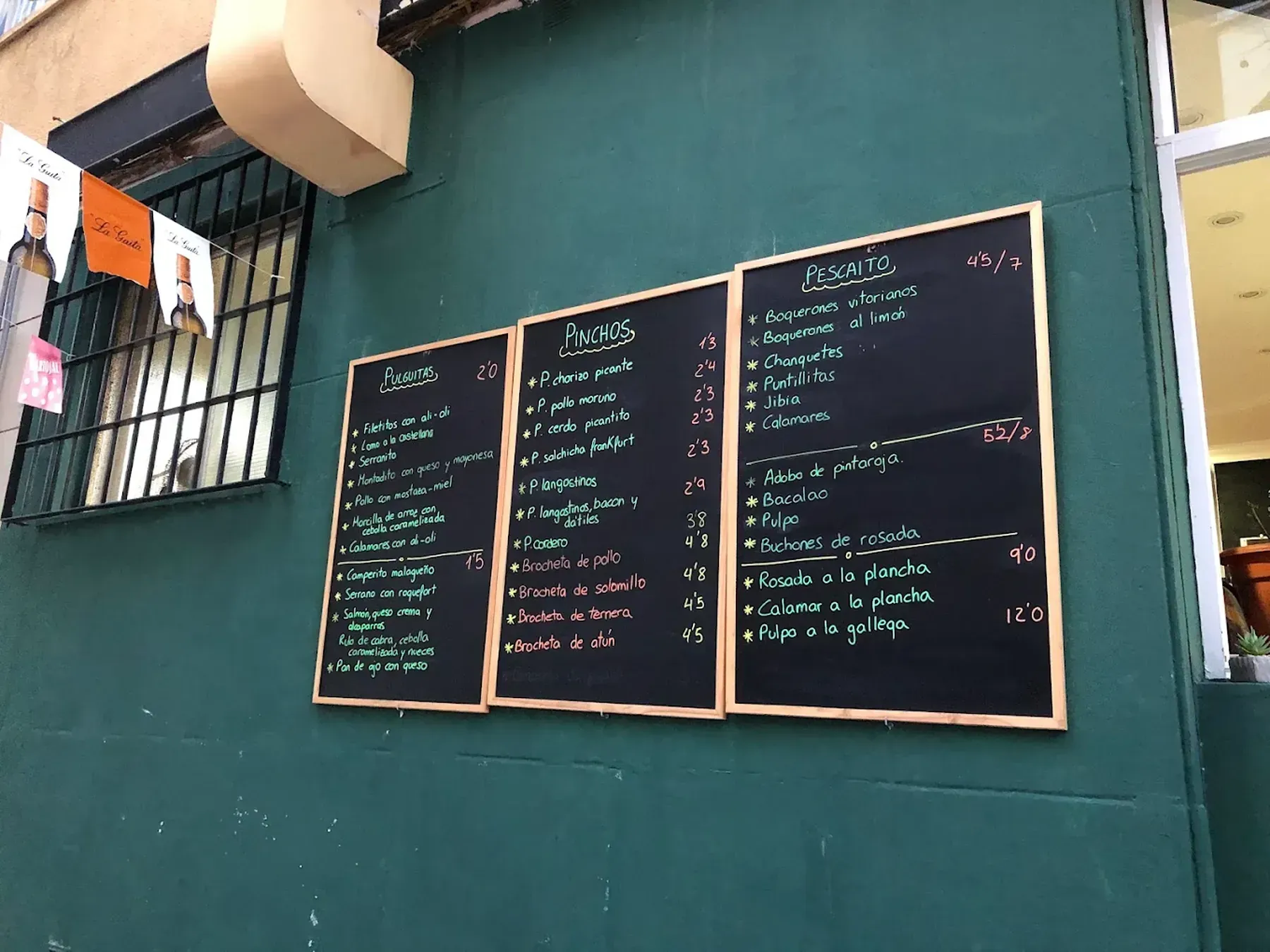 Tres menús de pizarra sobre una pared verde azulado; los platos están enumerados con tiza blanca.
