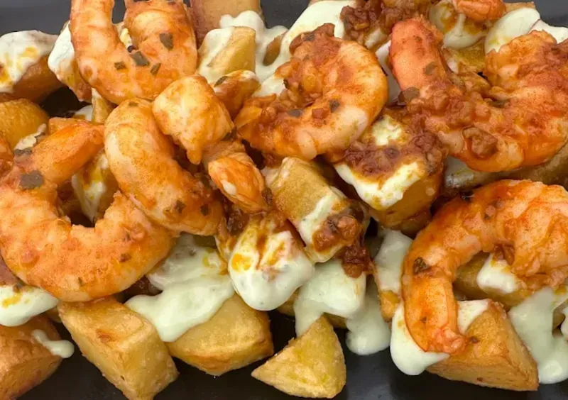 Papas fritas cubiertas con camarones y salsa blanca.