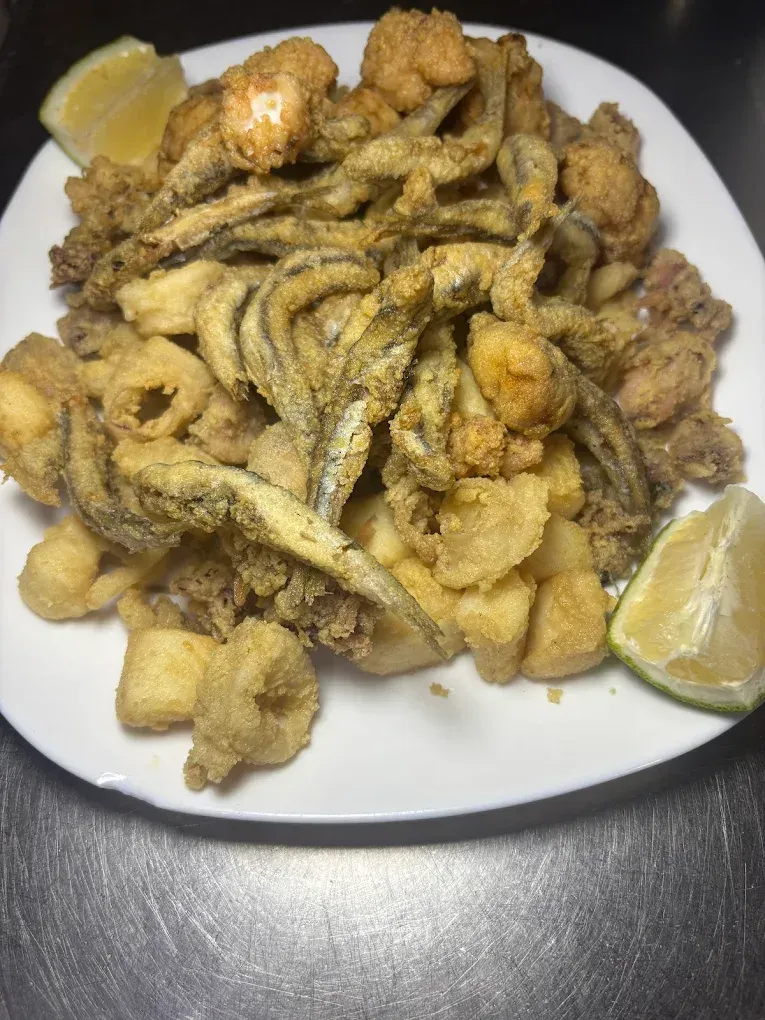 Un sándwich y un café en la mesa de una terraza. El sándwich lleva carne y patatas fritas.