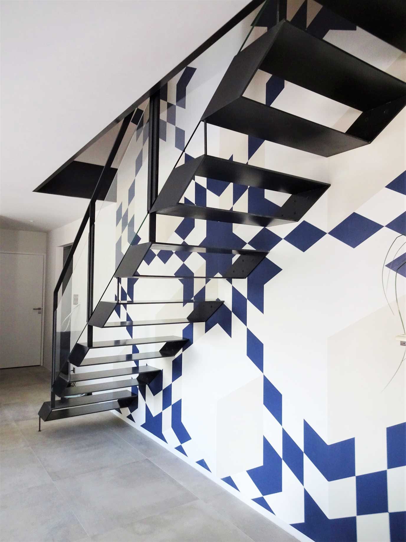 Escalier en acier et en verre au design contemporain et pan de mur aux motifs géométriques bleus et gris clair