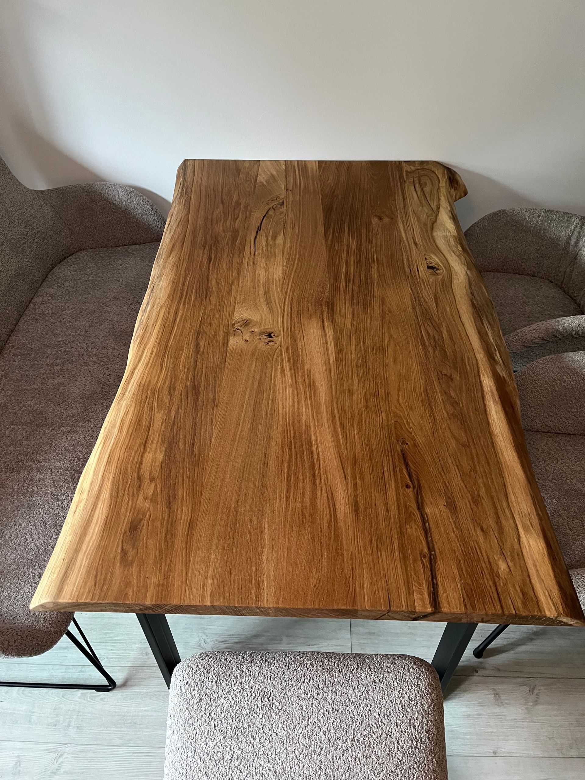 Holztisch mit dunklen Metallbeinen auf einer gemusterten Bank vor einem Sofa in neutralen Tönen.