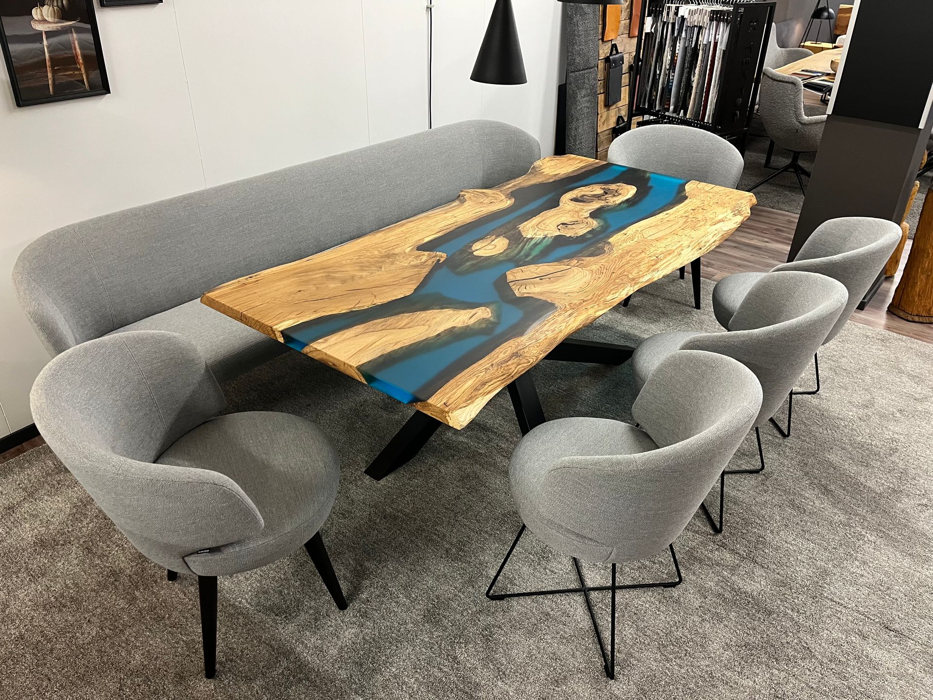 Esstisch mit blauem Harzfluss und sechs grauen Stühlen sowie einer langen grauen Bank.