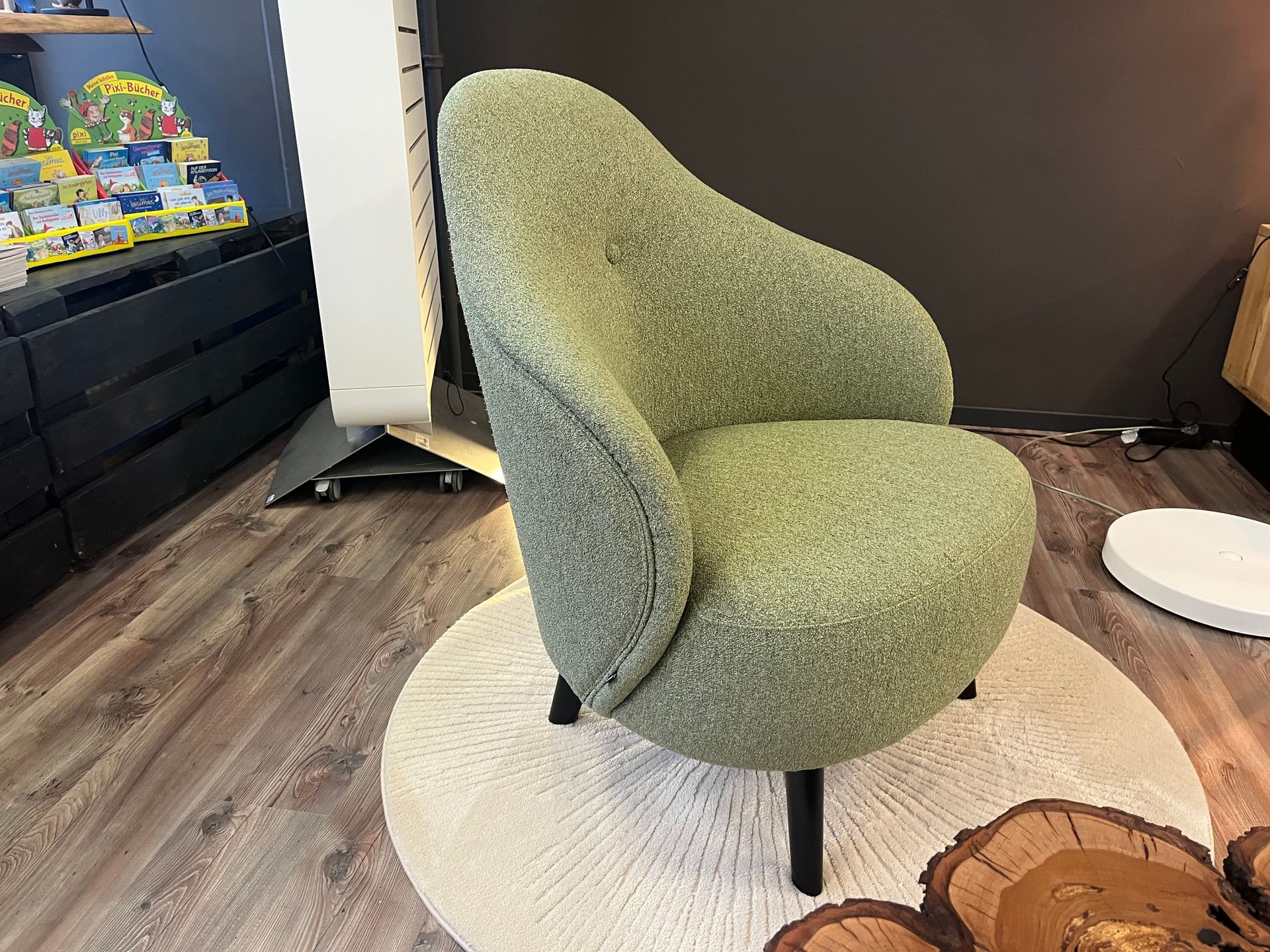 Grüner Bouclé-Sessel auf einem weißen runden Teppich, Holzboden.