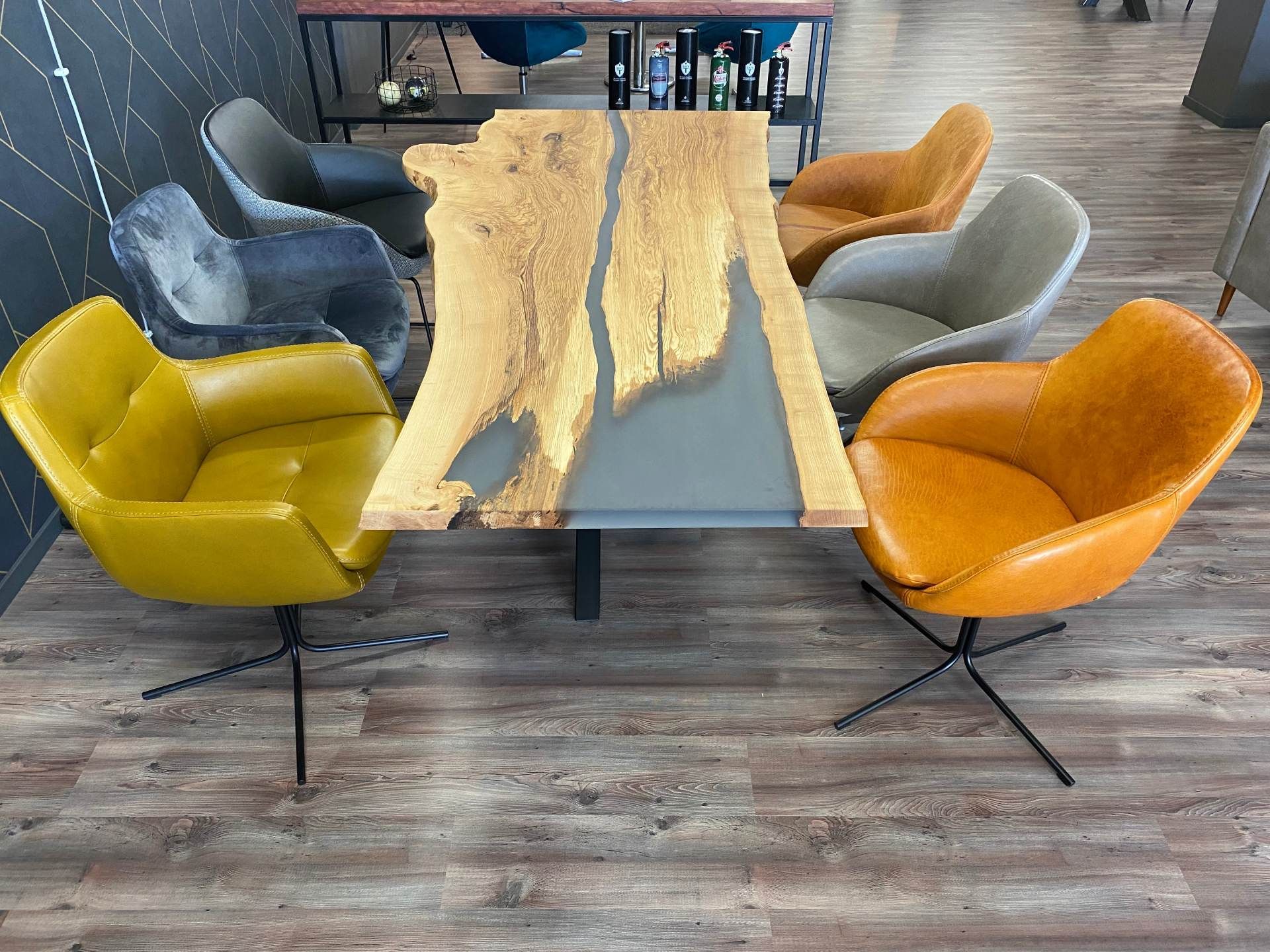 Ein Wohnzimmer mit einem langen handgefertigten Naturholz-Epoxidharztisch und unterschiedlich gepolsterten Stühlen