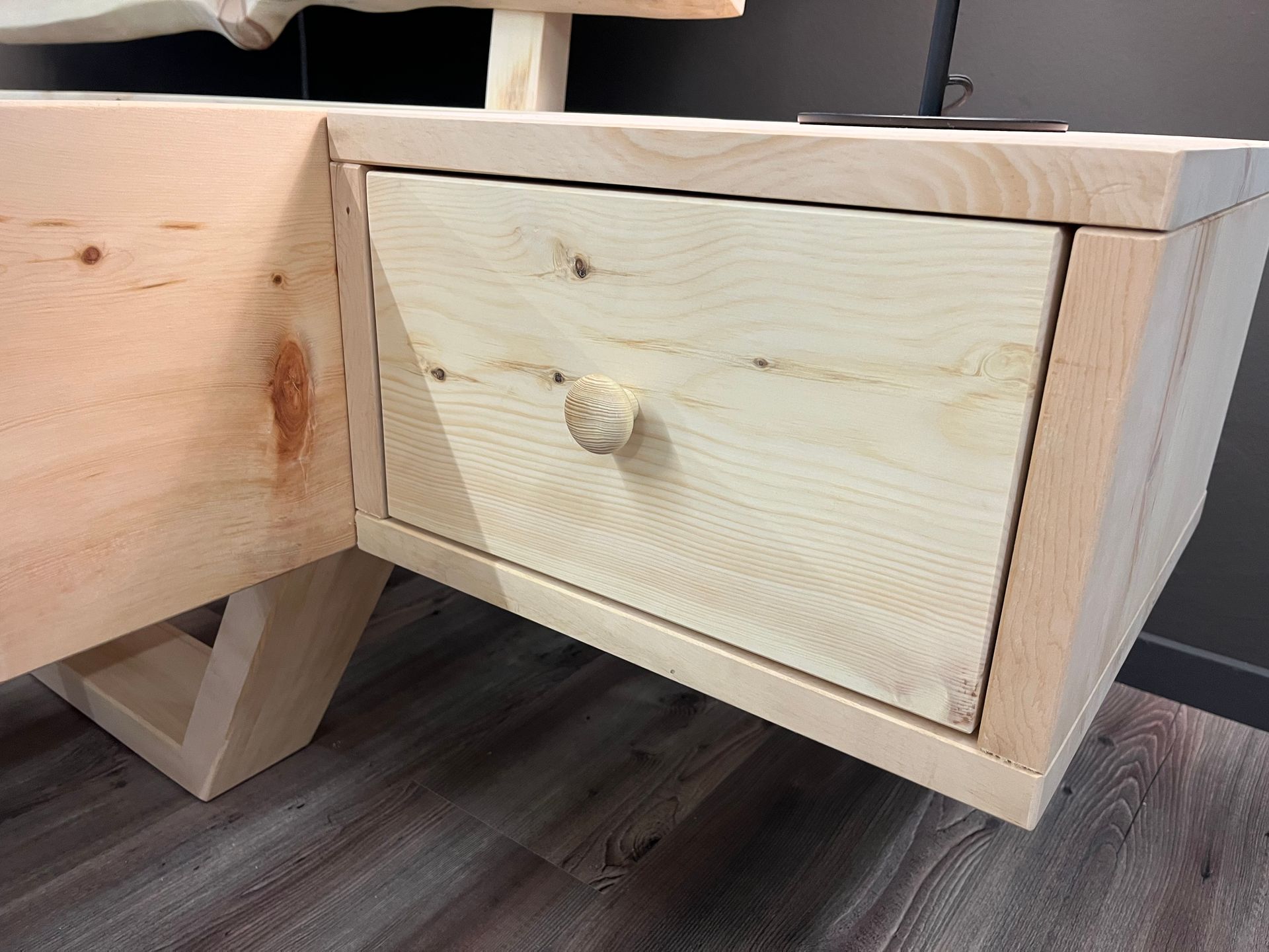 Auf einem Holzboden steht ein Nachttisch aus Holz mit einer Schublade darunter.