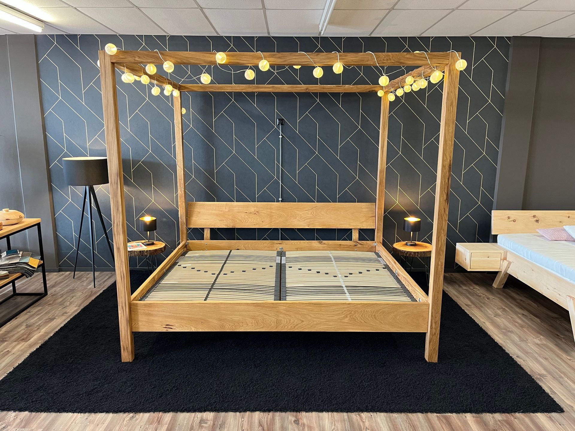 Himmelbett aus Holz mit Lichterkette in einem Ausstellungsraum.