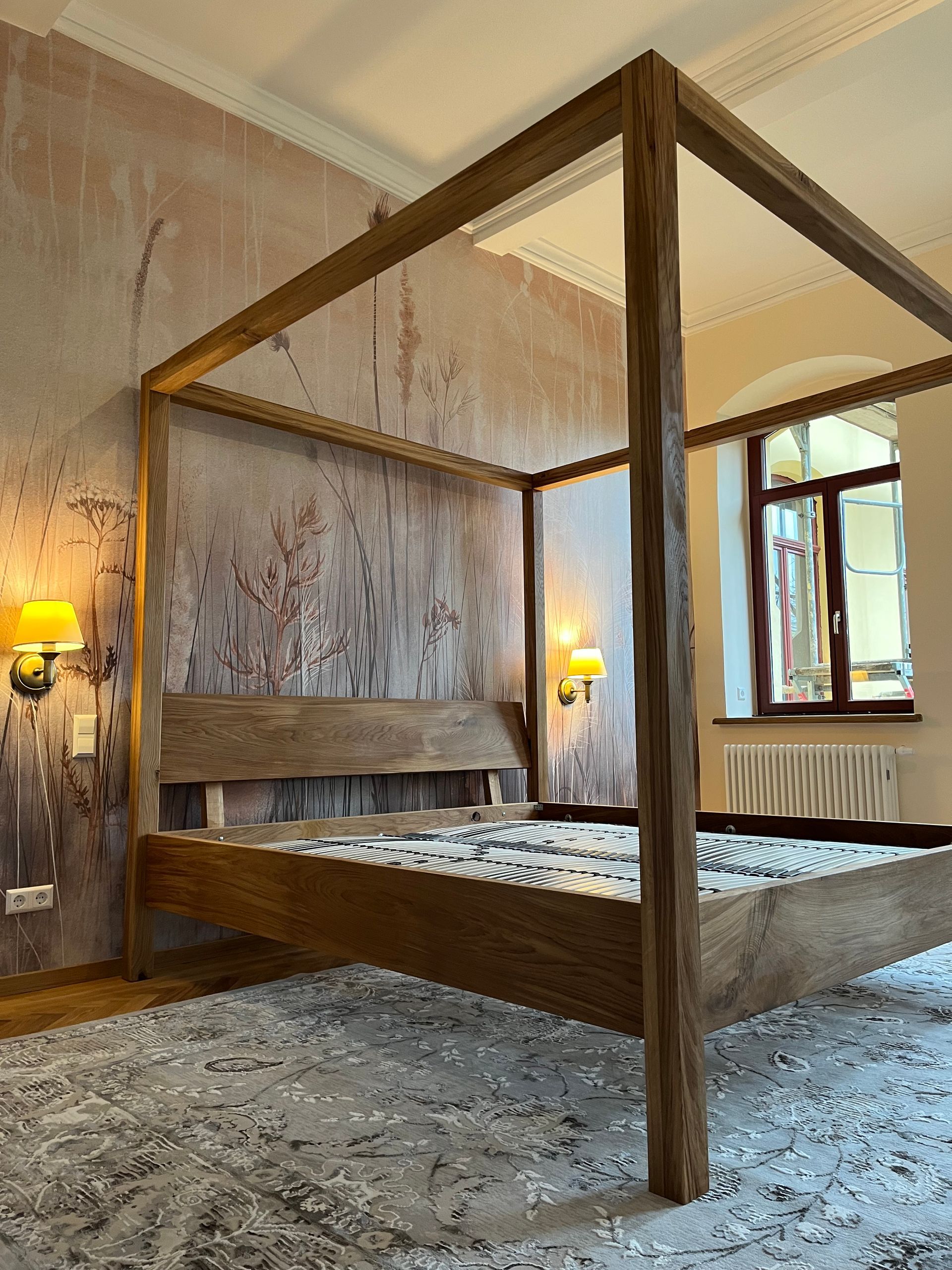 In einem Schlafzimmer neben einem Fenster steht ein Himmelbett aus Holz.