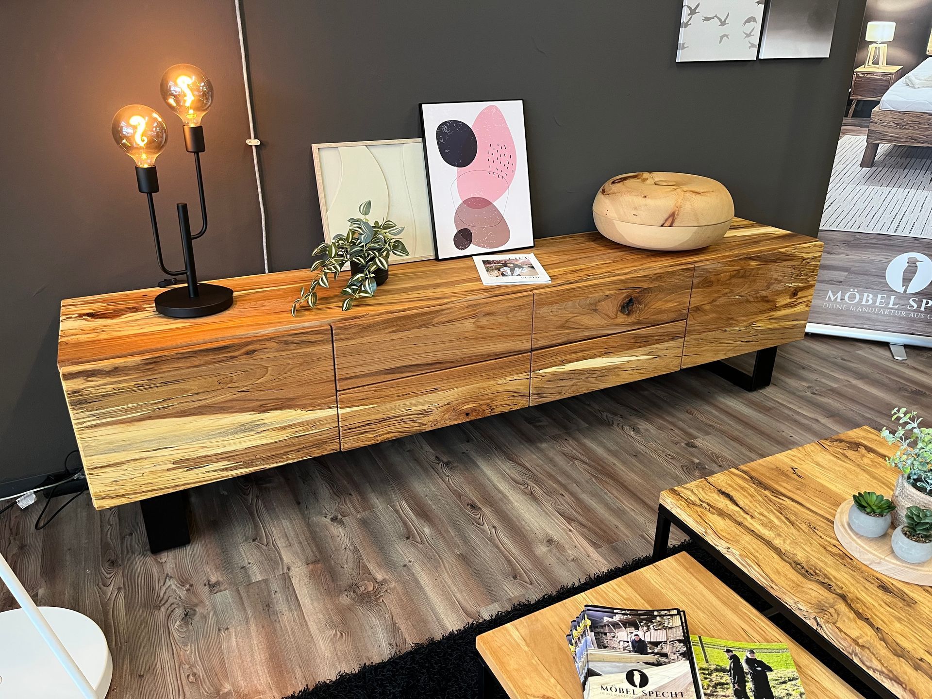 Ein hölzerner Präsentationstisch mit Dekoration, Lampen, Kunstwerken und einem runden Brotlaib in einem modernen Interieur