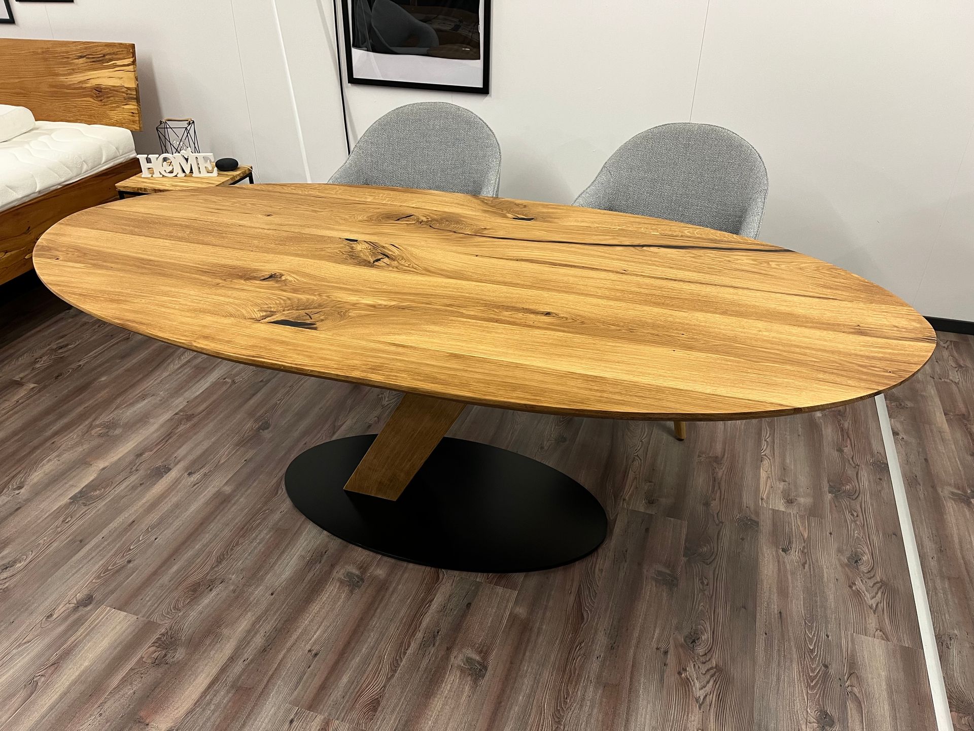 Ovaler Esstisch aus Holz mit schwarzem Gestell, zwei graue Stühle im Zimmer.