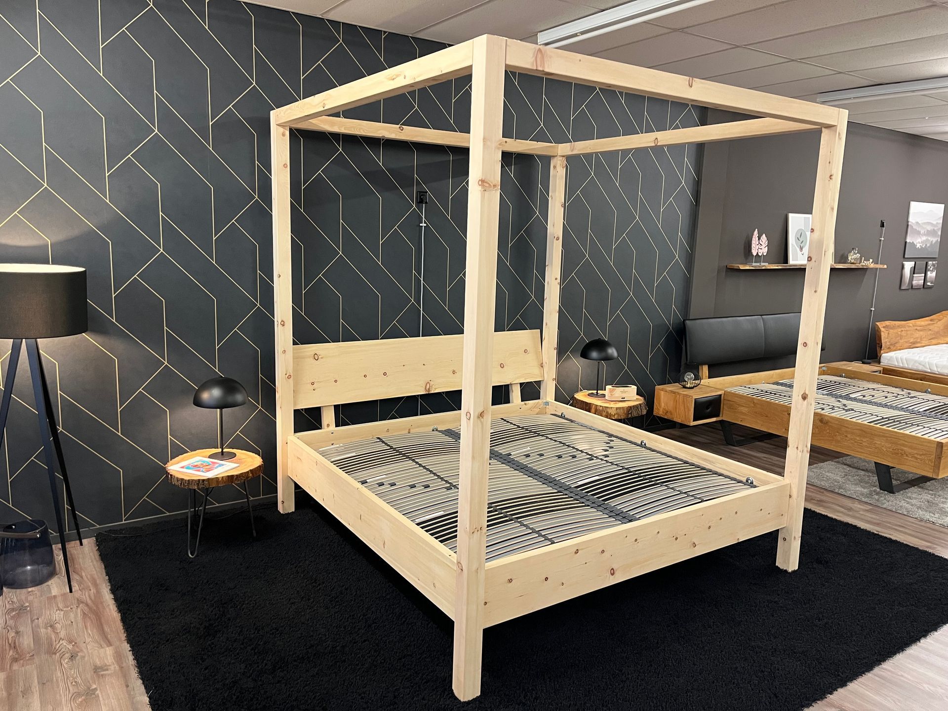 Himmelbett aus Holz in einem Zimmer mit schwarzem Teppich und geometrischer Tapete.