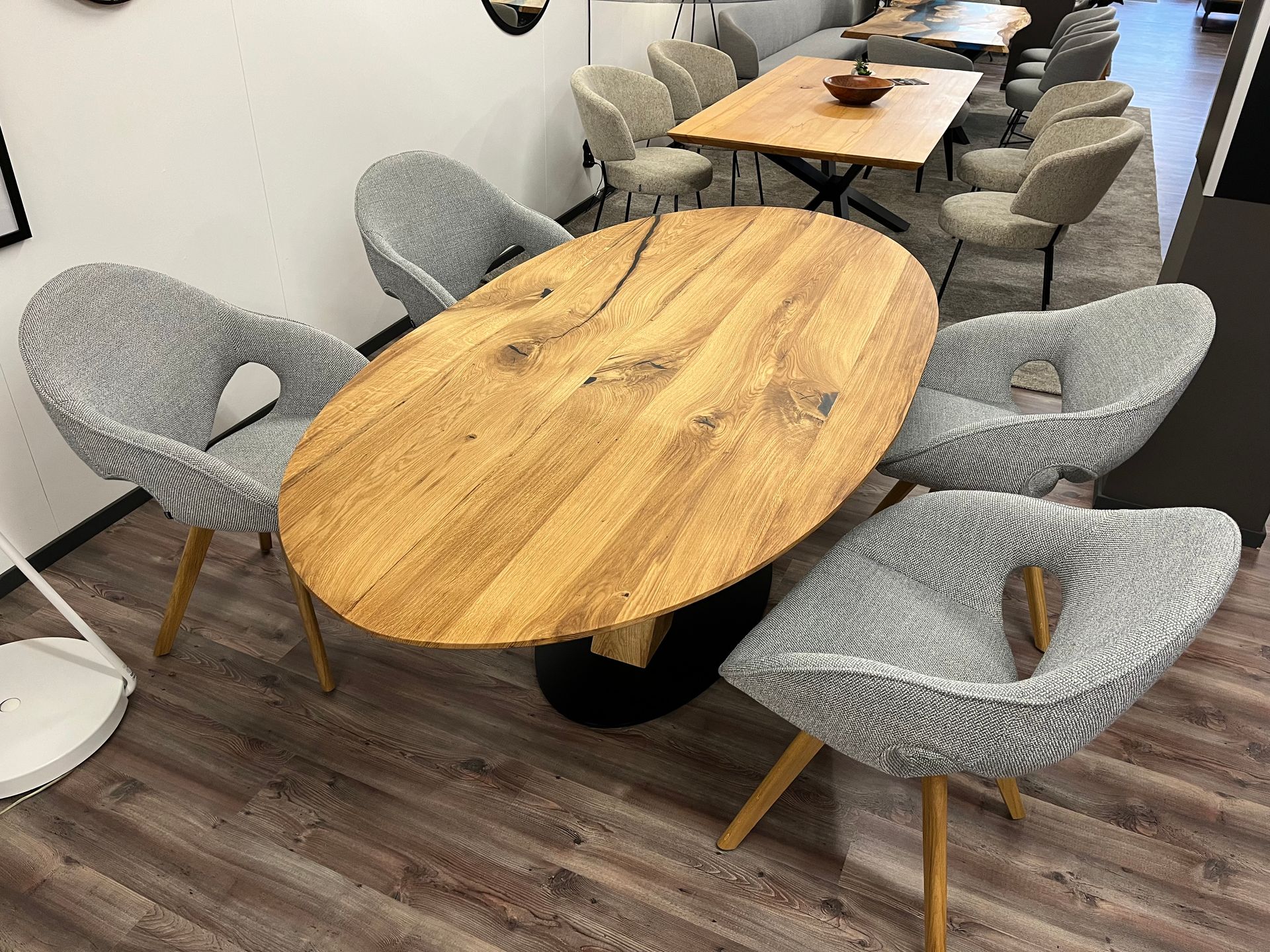 Ovaler Esstisch aus Holz mit vier grauen Polsterstühlen.