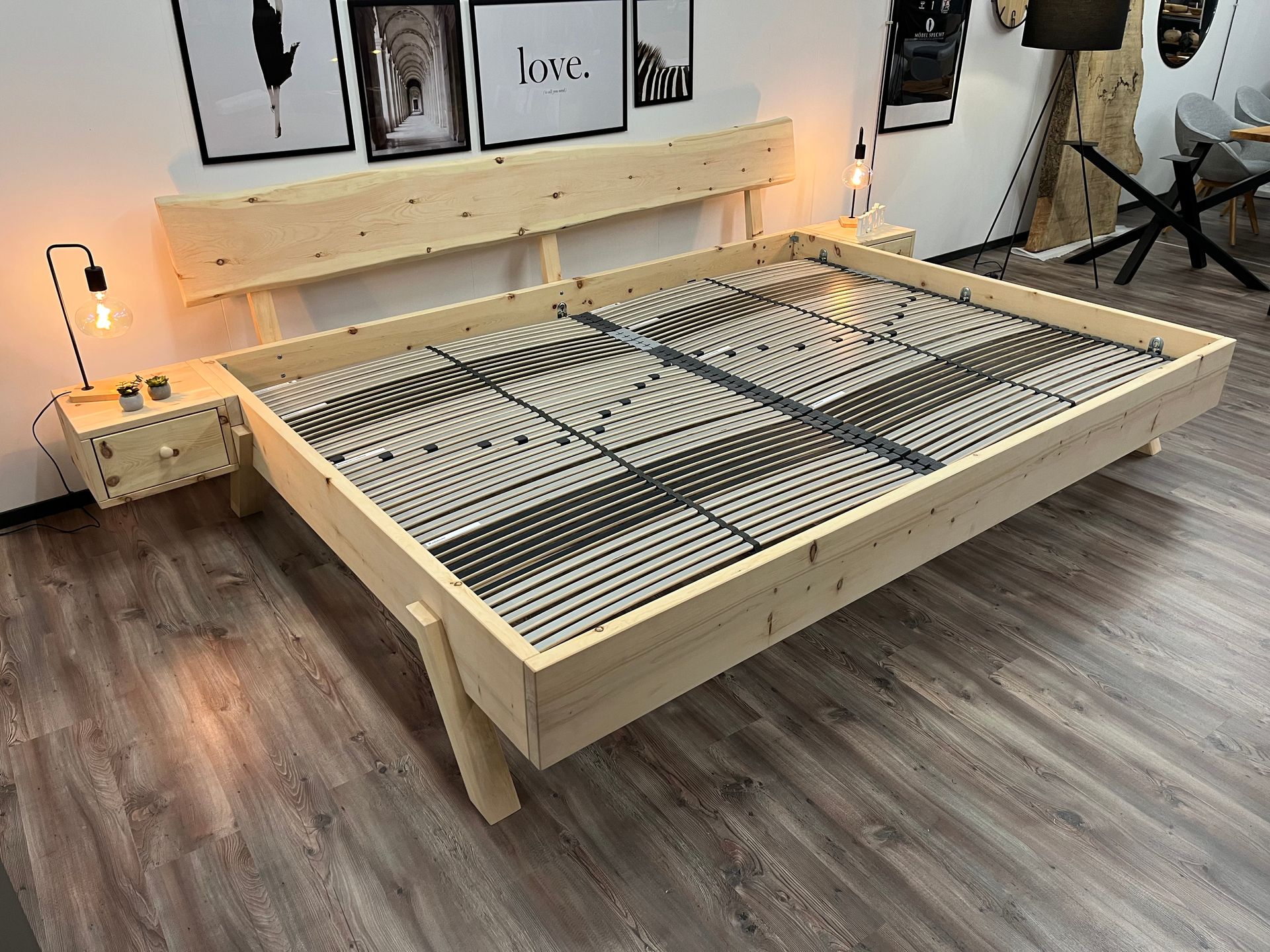 Holzbettgestell mit Kopfteil und Nachttisch, Zimmer mit gerahmten Kunstwerken, Holzboden und Lampen.