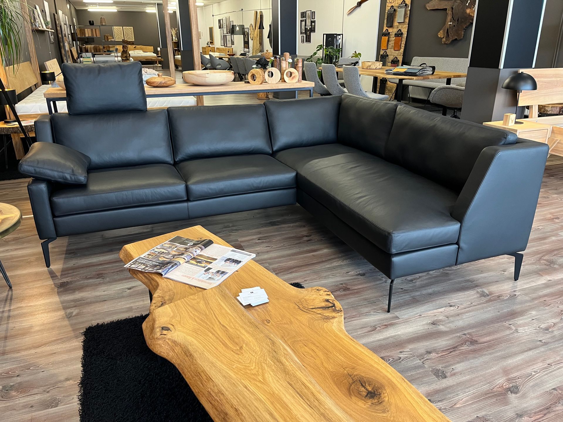 Schwarzes Leder-Ecksofa in einem Möbelhaus, davor ein hölzerner Couchtisch.