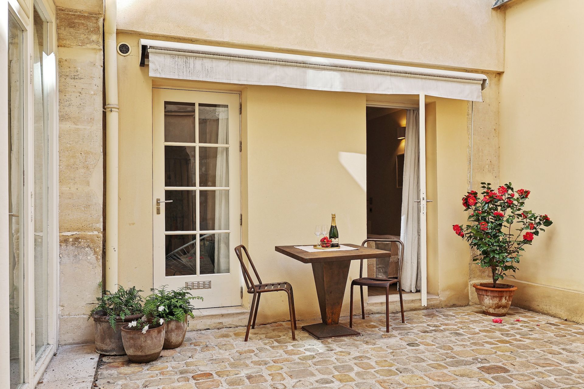 Courtyard with table, chairs, door, potted plants, and awning.