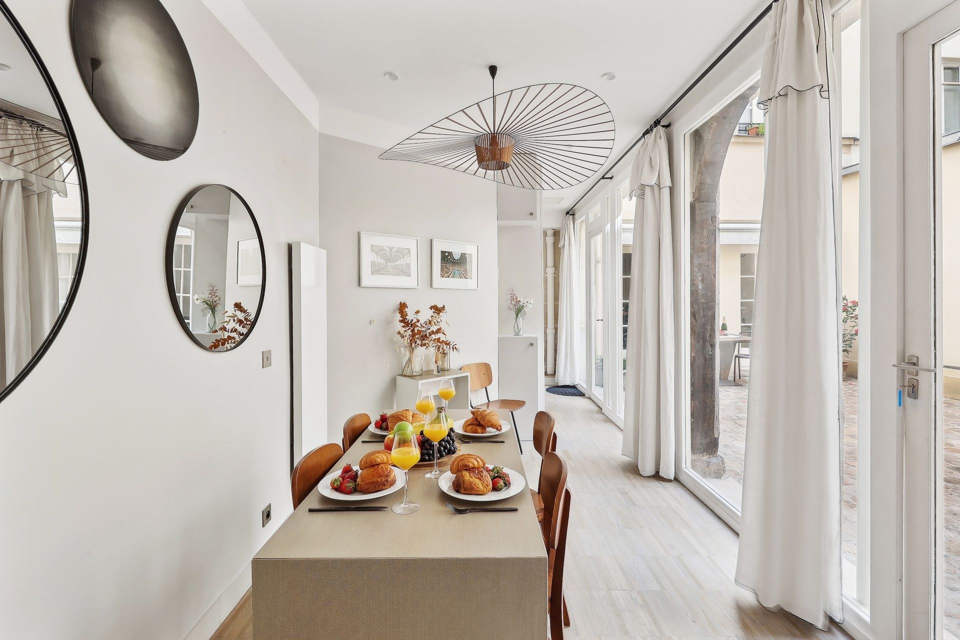 Dining room with table set for breakfast beside a wall of windows and mirrors.