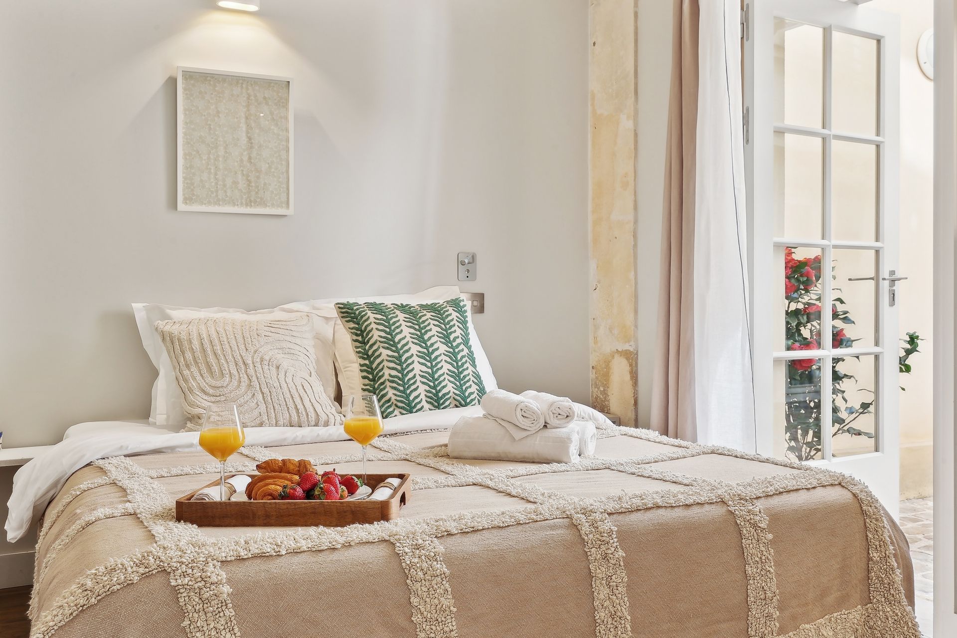 Bedroom with a bed, breakfast tray, and open French doors. Light beige and cream tones.
